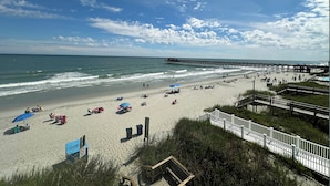 A beach with a pier, umbrellas, and beachgoers. - Dolphin Cove 3A - Oceanfront Condominium in Garden City Beach (Garden City)
