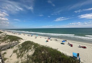Ein Strand mit einem hölzernen Promenadenweg, Strandstühlen und entspannten Menschen.