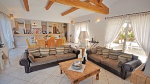 Un salon spacieux avec un grand canapé d’angle, une table basse en bois et une cuisine en arrière-plan.