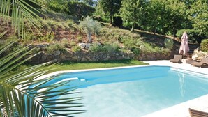 Une piscine entourée d’un jardin aménagé, avec un mur en pierre, un palmier et quelques chaises longues.
