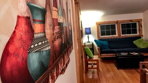 A living room with a large wall mural, a blue sofa, a wooden coffee table, and a small wooden chair. - Coburn On the Creek - Flyfish, Tube , Grill, Relax- PSU Football/Camp Woodward (Coburn)