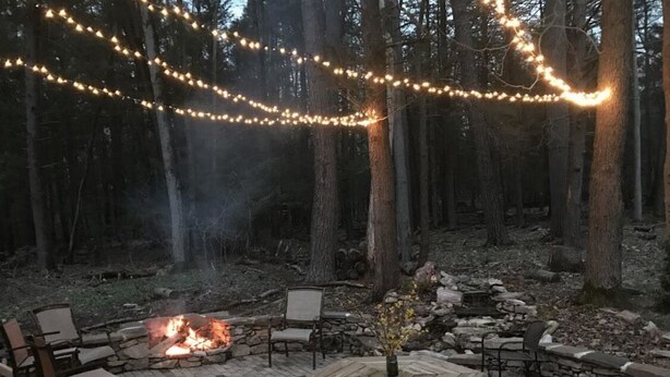 An outdoor patio with stone seating, a fire pit, and string lights. - Coburn On the Creek - Flyfish, Tube , Grill, Relax- PSU Football/Camp Woodward (Coburn)