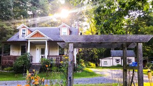 A two-story house with a porch, surrounded by a garden with various plants and flowers. - Coburn On the Creek - Flyfish, Tube , Grill, Relax- PSU Football/Camp Woodward (Coburn)
