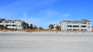 A beachfront property with multiple-story buildings featuring balconies, a sandy beach in the foreground, and a clear blue sky. - Sea Cloisters I 101B - Oceanfront Condominium in Surfside Beach (Surfside Beach)