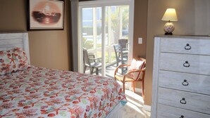 A bedroom with a bed, a dresser, a chair, and a balcony with chairs. - Sea Cloisters I 101B - Oceanfront Condominium in Surfside Beach (Surfside Beach)