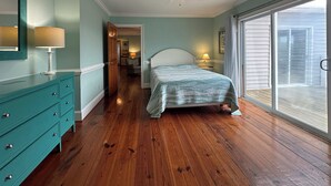 Una camera da letto con pavimento in legno, un letto con testiera bianca, una cassettiera verde acqua, una ventola a soffitto e vista sull'esterno tramite una porta scorrevole in vetro.