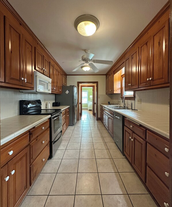 A kitchen with wooden cabinets, a microwave, stove, and a ceiling fan.