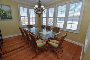 Uma sala de jantar com mesa de vidro, cadeiras de vime e um candelabro.