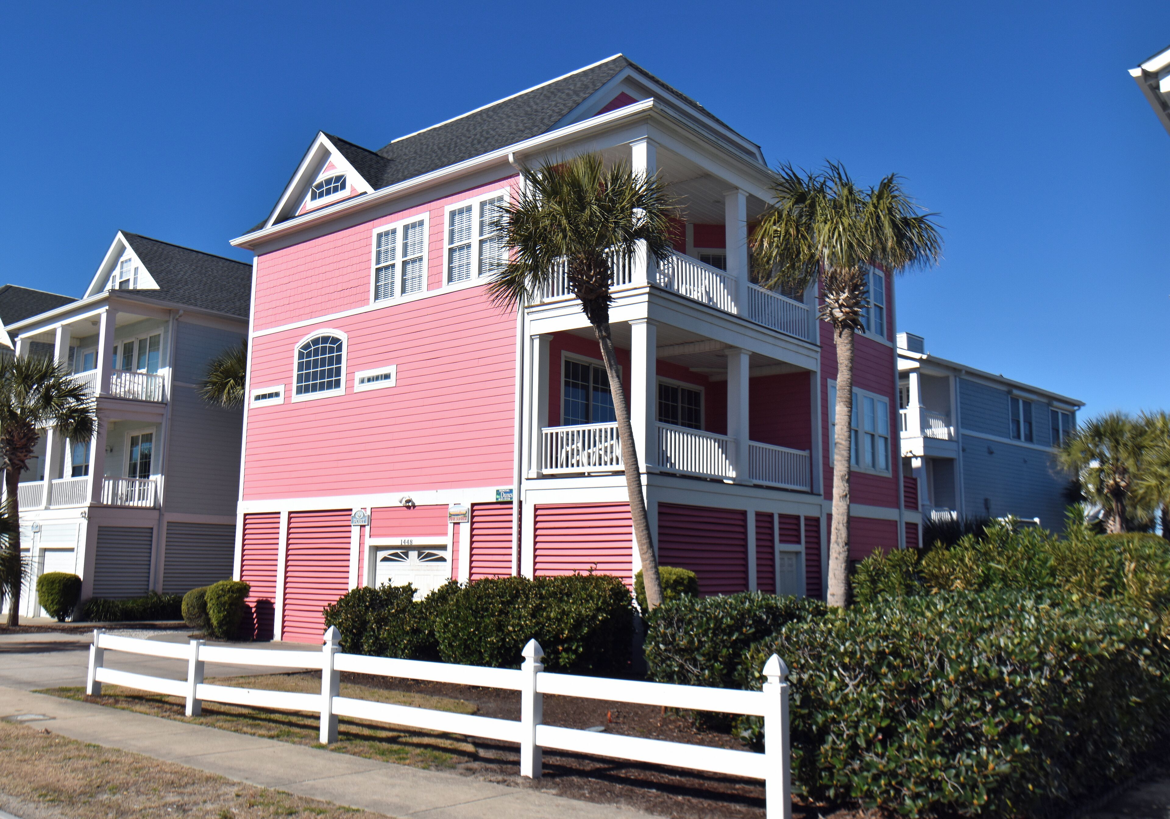 A pink two-story house with a white porch and a white fence in front.