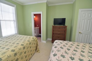 Quarto com duas camas, uma televisão sobre suporte e uma porta.