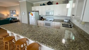 A modern kitchen with white cabinets, a granite countertop, a built-in oven, and a stainless steel sink. There are three wooden stools at the island.