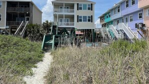 A beachfront property with a sandy path leading to a two-story building with a balcony.