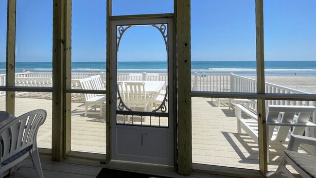 Een terras aan het strand met witte stoelen en een houten reling, met uitzicht op de oceaan.