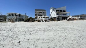 Een pand aan het strand met meerdere gebouwen, waaronder een groot huis met balkon en een kleinere constructie met een trap naar een terras.