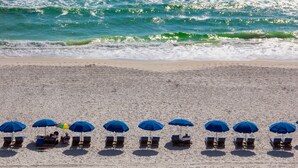 A beach with rows of blue umbrellas and wooden lounge chairs.