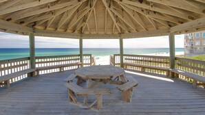 A wooden gazebo with a picnic table and benches, overlooking a beach and ocean.