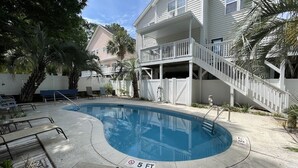 A swimming pool with a 5 ft depth limit, surrounded by a concrete deck with lounge chairs and a staircase leading to a building with a balcony. - Tucked Inn 2.0 - Walk to Beach Triplex in Surfside Beach (Surfside Beach)