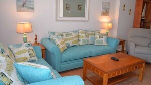 A living room with a blue sofa set, two lamps, a wooden coffee table, and a framed picture on the wall. - Tucked Inn 2.0 - Walk to Beach Triplex in Surfside Beach (Surfside Beach)