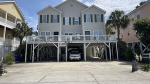 A two-story building with a covered parking area and a white car parked inside. - Tucked Inn 2.0 - Walk to Beach Triplex in Surfside Beach (Surfside Beach)