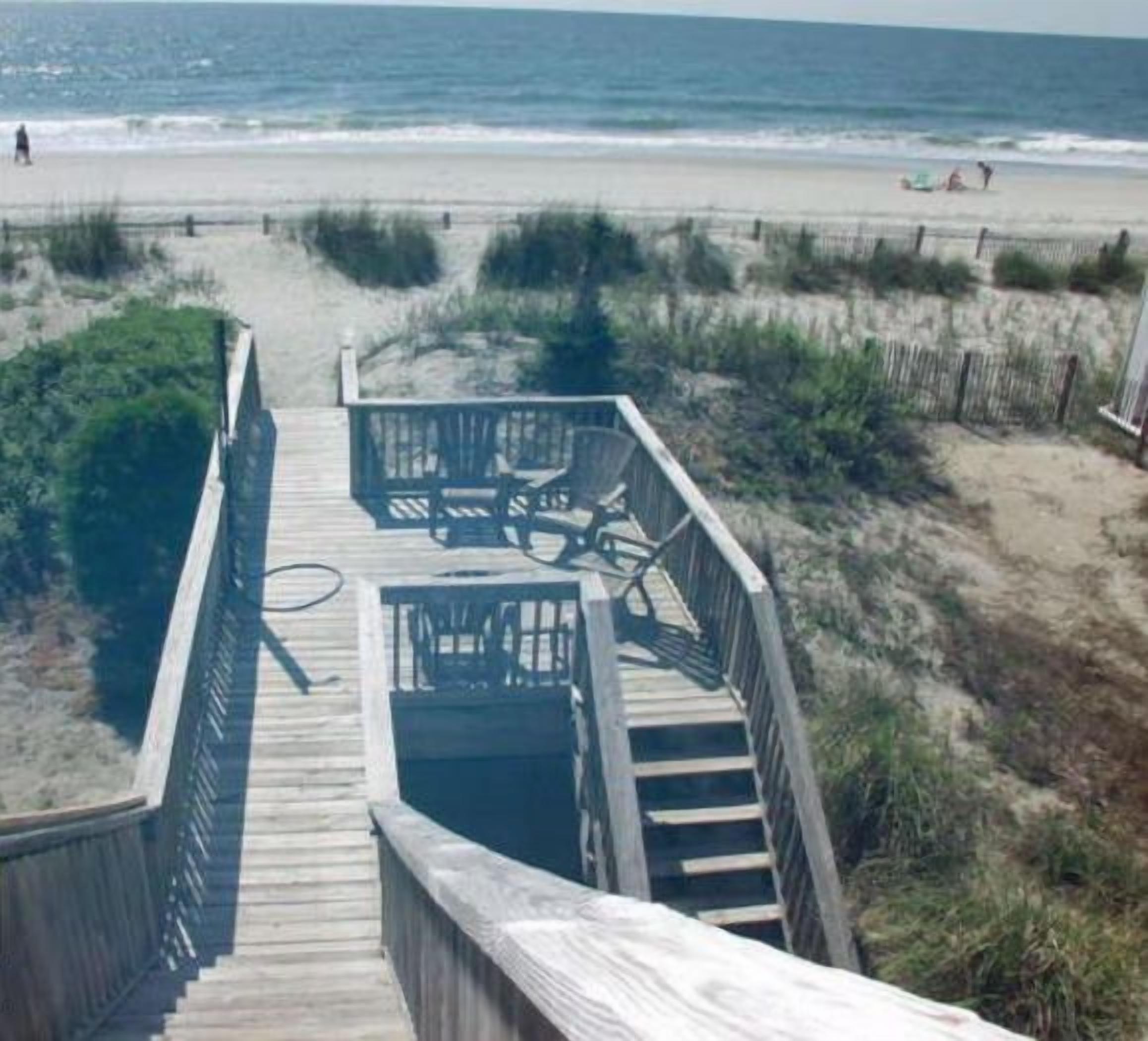 A wooden boardwalk leading to a beach with a dune rental sign.