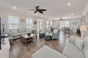 A spacious living room with a wooden floor, a sofa, a coffee table, and a dining area with chairs and a table. - Buckeye Heaven - Second Row in Garden City Beach (Garden City Beach)