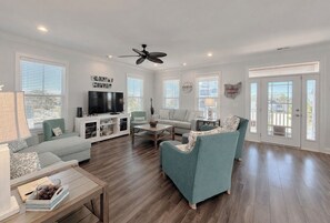 A spacious living room with a flat-screen TV, a ceiling fan, and a large window with blinds. - Buckeye Heaven - Second Row in Garden City Beach (Garden City Beach)