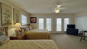 Une chambre avec deux lits, un ventilateur de plafond, une télévision et une commode.