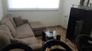 Uma sala de estar com sofá seccional, mesa de centro de vidro e um armário preto com tampo de vidro.