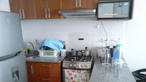 Cozinha compacta com armários de madeira, fogão de aço inoxidável e uma geladeira pequena.