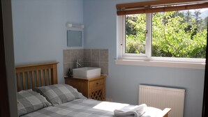 A bedroom with a bed, a bedside table with a sink, a window with a view of greenery, and a radiator. - Comfortable property with ample space and views of the 5 sisters of Kintail (Glenshiel)