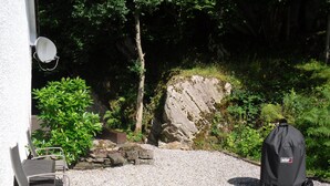 A patio area with a grill, a chair, and a stone wall. - Comfortable property with ample space and views of the 5 sisters of Kintail (Glenshiel)