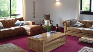 A living room with two leather sofas, a wooden coffee table, and a red carpet. - Comfortable property with ample space and views of the 5 sisters of Kintail (Glenshiel)