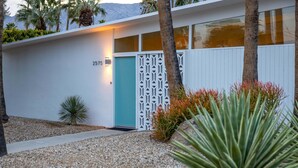 A modern building with a teal door, numbered 2575, white walls, and a decorative white fence. - Desert Eden – Midcentury Pool Oasis (Palm Springs)