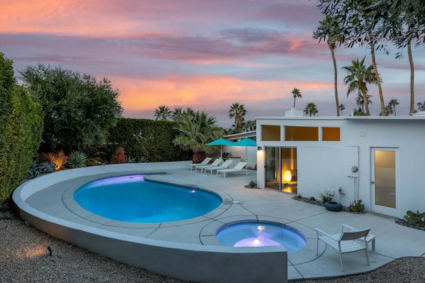 A modern pool area with a circular pool, lounge chairs, and a small outdoor kitchen.