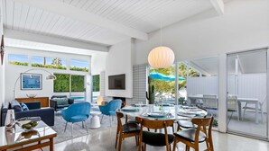 A modern interior with a dining area, a sofa, and a TV. - Desert Eden – Midcentury Pool Oasis (Palm Springs)
