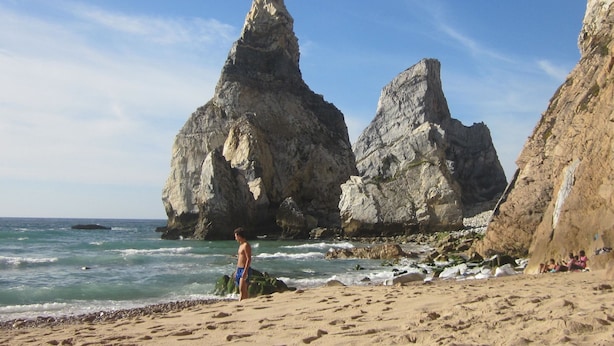 Ein Strand mit Felsformationen und einer Person, die am Sand steht.