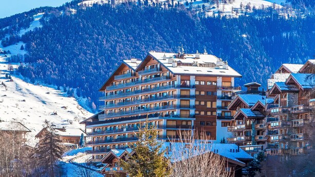 Een hotel met meerdere verdiepingen en balkons, met een besneeuwd berglandschap op de achtergrond.