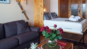 Een gezellige kamer met een bank, een bed met witte lakens en een vaas met rode bloemen op een houten tafel.