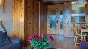 Een houten interieur met een bank, een eettafel met stoelen, en een vaas met bloemen.