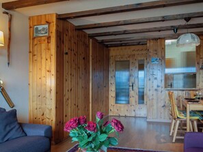A wooden interior with a sofa, a dining table with chairs, and a vase of flowers.