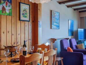 Un coin repas avec des murs en bois, une table dressée pour deux personnes et un téléviseur en arrière-plan.