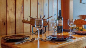 Een houten eettafel gedekt met borden, bestek en wijnglazen, met een fles wijn en een houten kan op tafel.