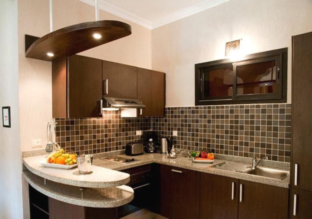 A modern kitchen with dark wooden cabinets, a curved granite countertop, a built-in microwave, and a stainless steel sink.