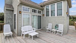 A house with a deck, white outdoor furniture, and a large window. - The Taylor at Ships Watch in Duck (Duck)
