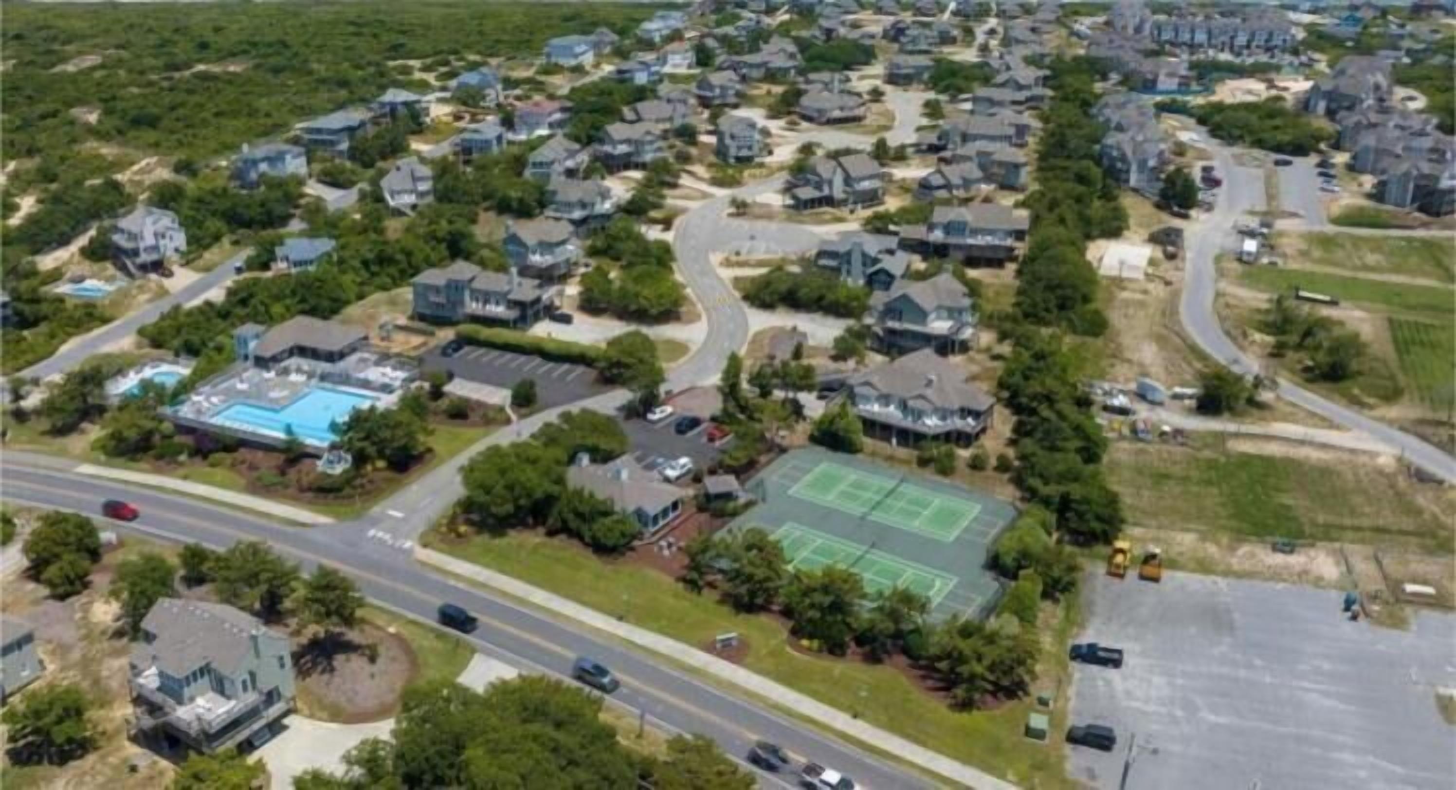An aerial view of a residential area with houses, a swimming pool, and a tennis court.