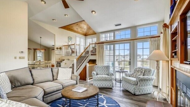 A spacious living room with a large sofa, two armchairs, a coffee table, and a fireplace. A staircase leads to an upper level. - The Taylor at Ships Watch in Duck (Duck)