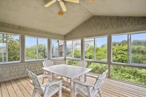 A sunroom with a table and chairs, large windows, and a view of greenery. - The Taylor at Ships Watch in Duck (Duck)