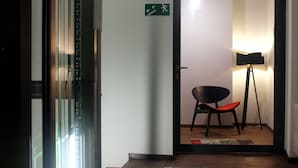 An interior hallway with a door leading to a room, a chair, a standing lamp, and a patterned rug. - Dada Premium Aparthotel (Kraków)