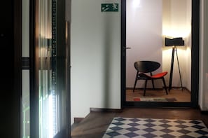An interior hallway with a door leading to a room, a chair, a standing lamp, and a patterned rug. - Dada Premium Aparthotel (Kraków)
