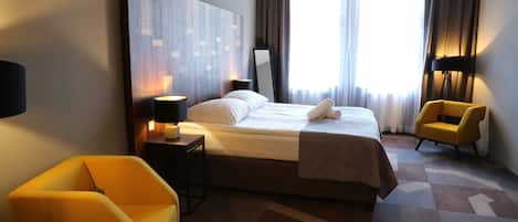 A hotel room with a large bed, a bedside table with a lamp, a chair, and a large mirror.